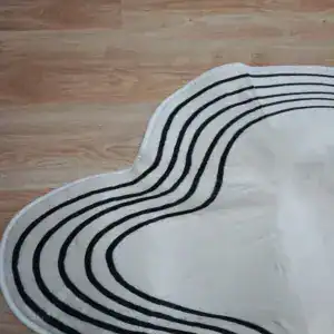 Alfombra blanca con líneas negras onduladas, vista de cerca sobre madera