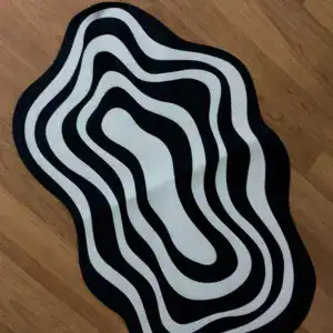 Alfombra de baño de formas onduladas en blanco y negro sobre suelo de madera