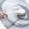 Alfombra baño gris y blanca siendo limpiada con esponja y jabón.