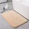 Alfombra de baño suave beige rectangular en baño con azulejos grises.