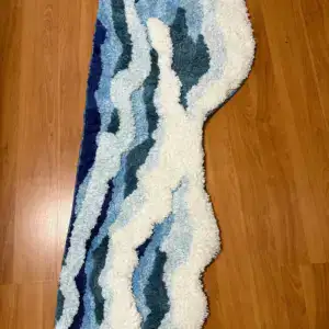 Alfombra de pelo con relieve de olas azules y blancas sobre suelo de madera