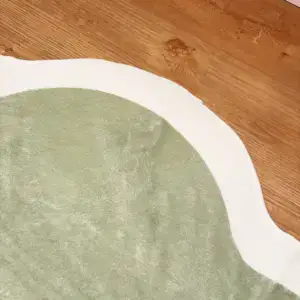 Alfombra verde salvia con borde blanco ondulado sobre suelo de madera